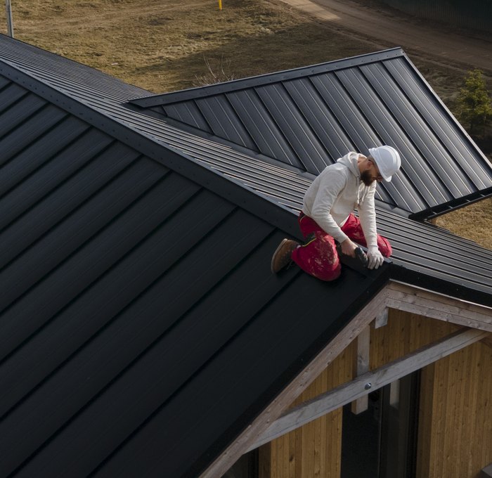 Roofer sitting on the ridge of a dark standing-seam roof