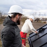 Two roofers fitting a standing-seam panel